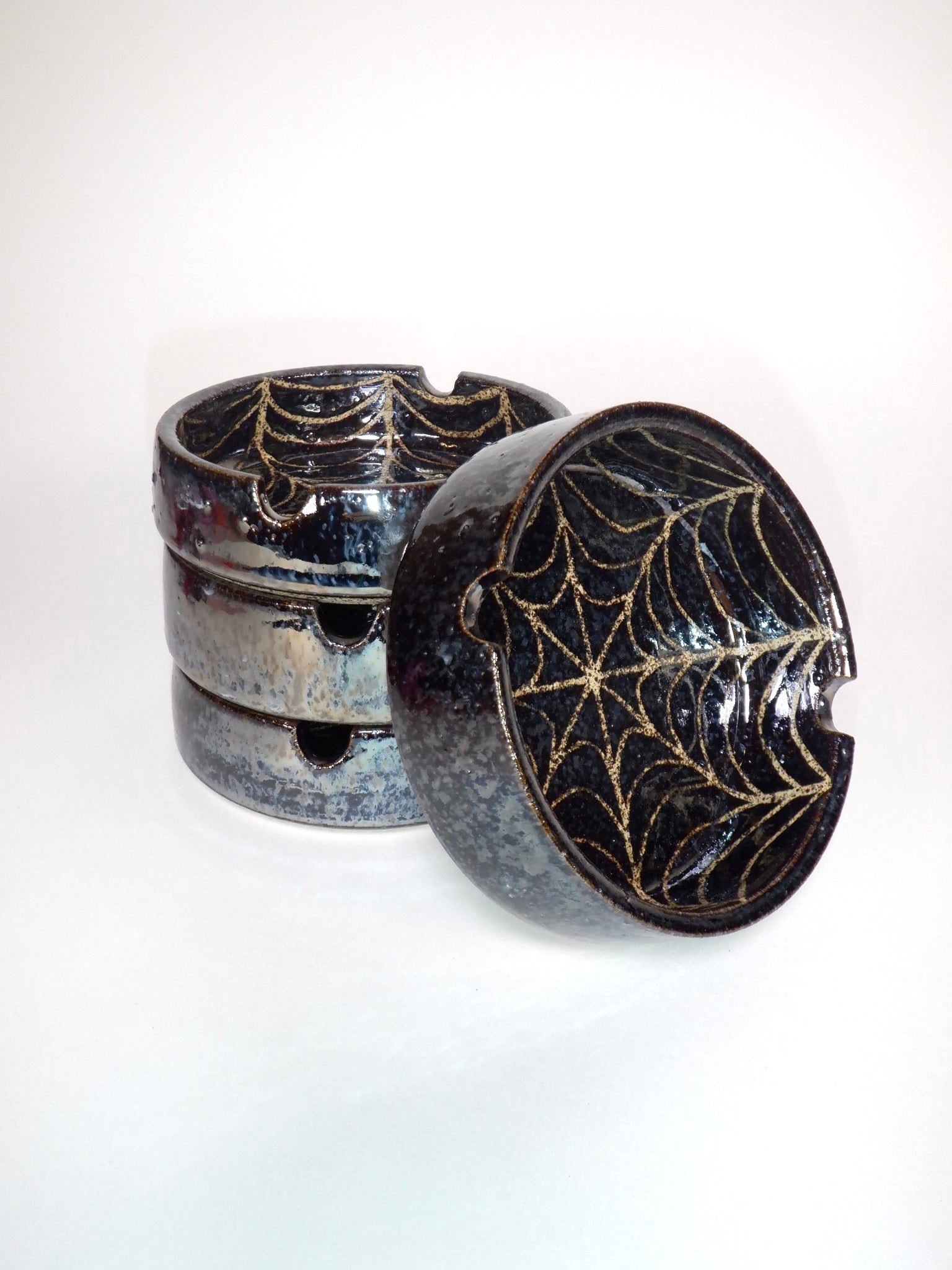 Black ceramic ash tray with spider web design on a white background