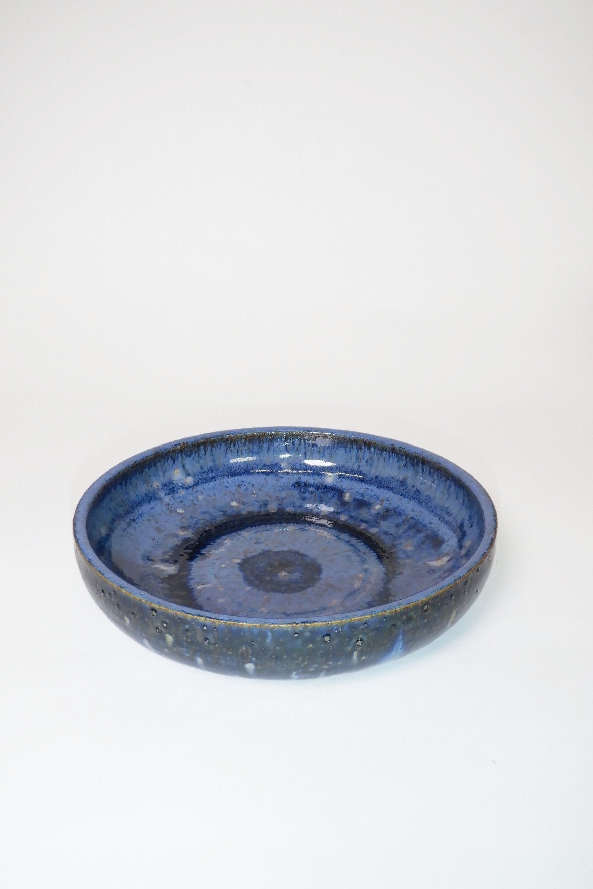 A round ceramic shallow dish with a textured, speckled cobalt blue glaze, photographed against a seamless white background.