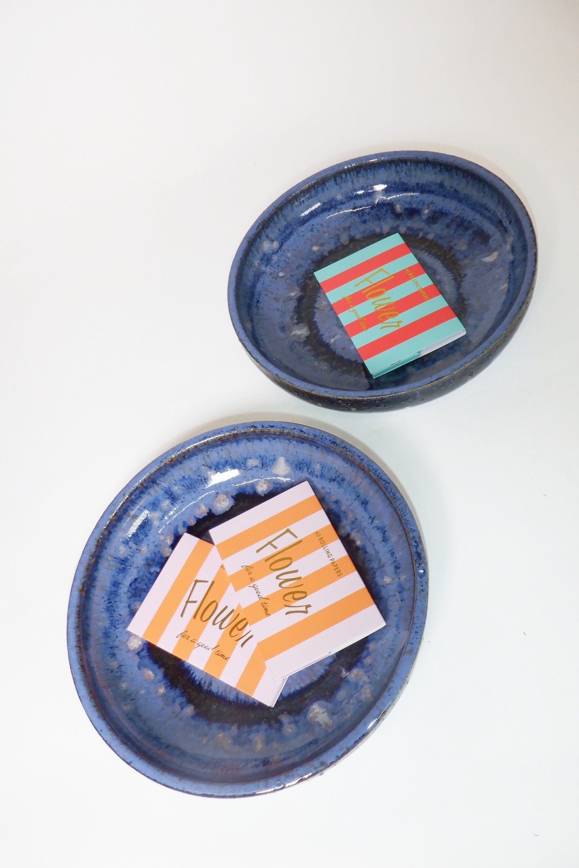 Two round blue ceramic plates with a glossy, marbled finish, each holding a small striped paper flower card, displayed on a clean white background.